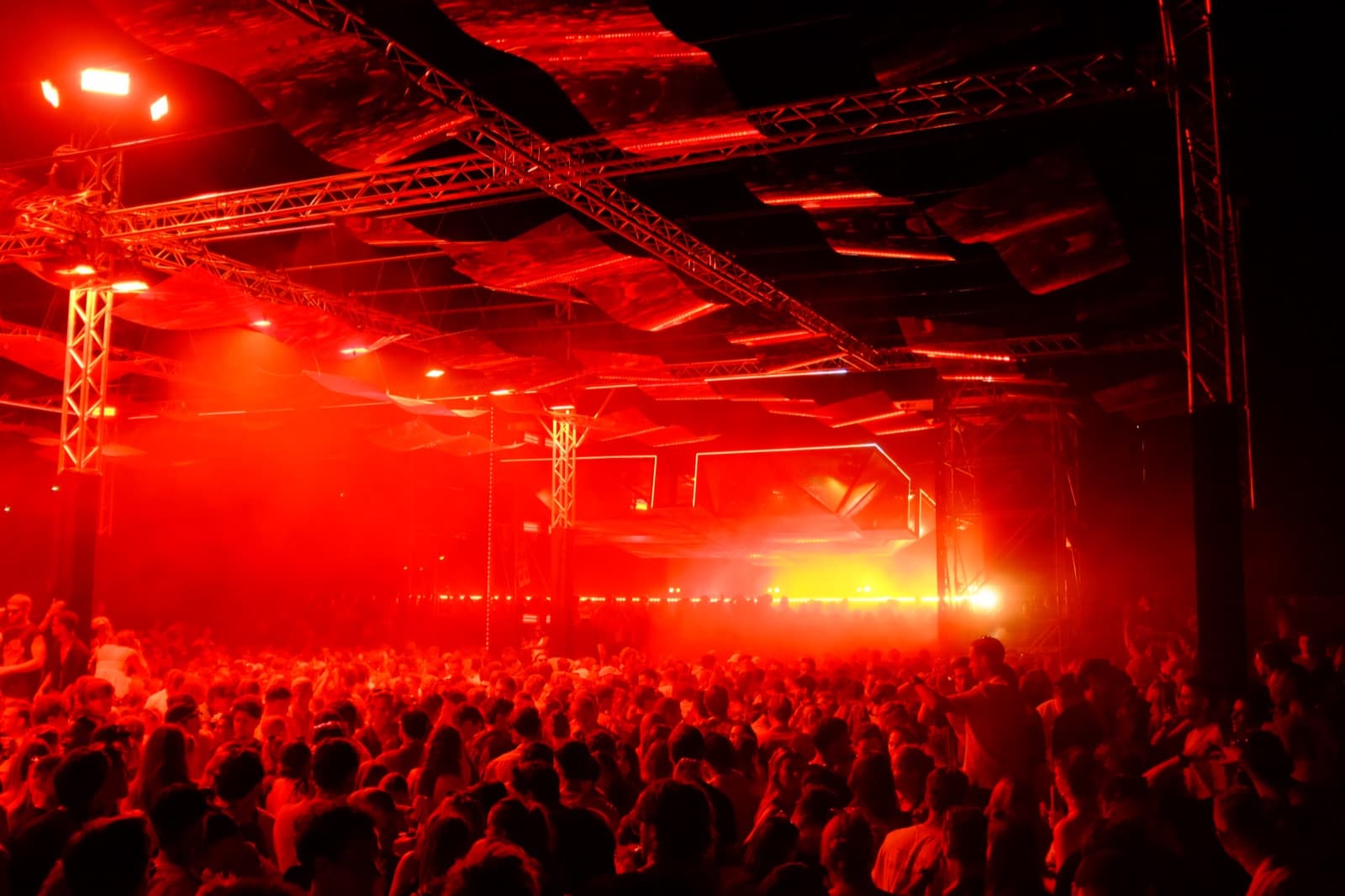 A packed venue lit in deep red, with truss, LED battens, and moving heads rigged overhead.